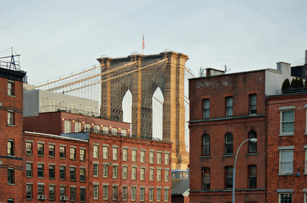 Brooklyn Bridge behind downtown buildings as viewed from along the side streets of downtown Manhattan.